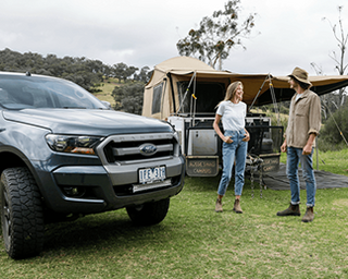 Two people standing next to a Ford truck with a camper shell in a grassy area.